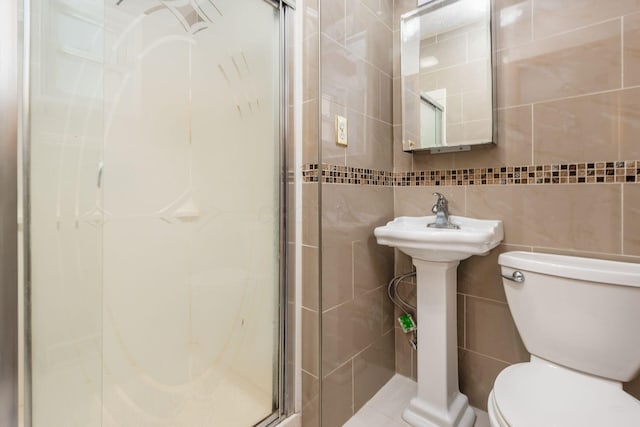 bathroom with tile walls, toilet, and a shower with shower door