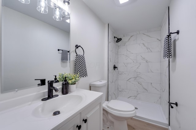 bathroom with tiled shower, hardwood / wood-style floors, vanity, and toilet