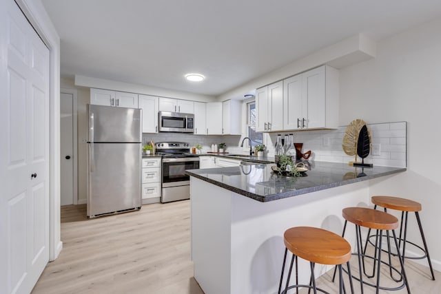 kitchen featuring kitchen peninsula, a breakfast bar, tasteful backsplash, white cabinetry, and appliances with stainless steel finishes