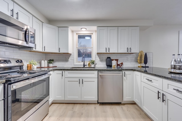 kitchen featuring white cabinets, dark stone countertops, stainless steel appliances, decorative backsplash, and sink