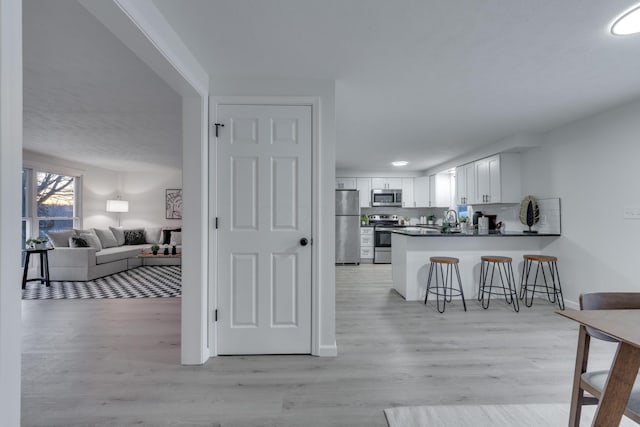 kitchen with a kitchen breakfast bar, light hardwood / wood-style floors, stainless steel appliances, kitchen peninsula, and white cabinetry