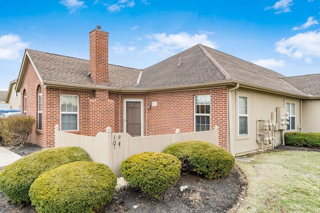 back of property featuring brick siding, a chimney, a shingled roof, and fence