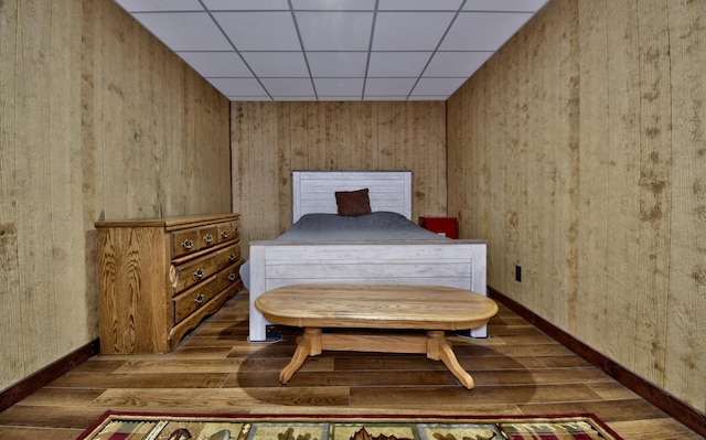 bedroom featuring a paneled ceiling, wooden walls, and dark wood-type flooring