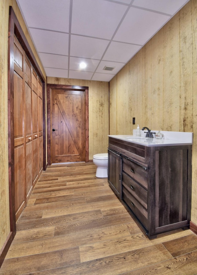 bathroom featuring toilet, a paneled ceiling, wooden walls, vanity, and hardwood / wood-style flooring