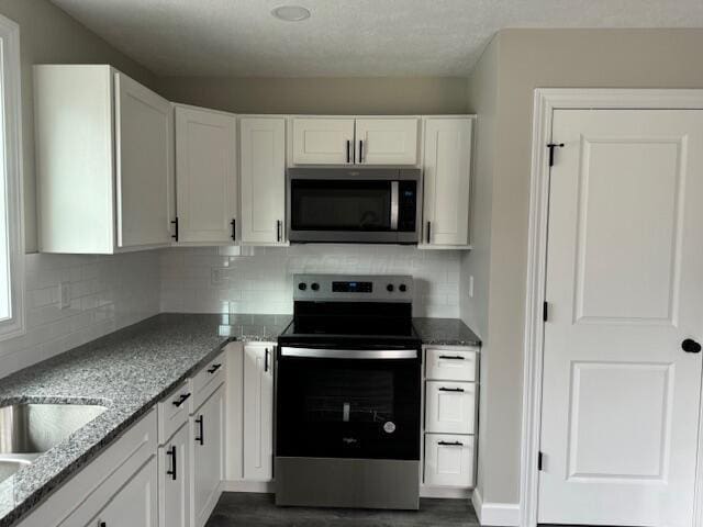 kitchen featuring white cabinetry, dark wood-type flooring, light stone counters, and appliances with stainless steel finishes