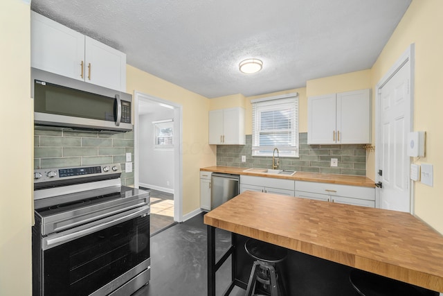 kitchen featuring wood counters, appliances with stainless steel finishes, a textured ceiling, sink, and white cabinets