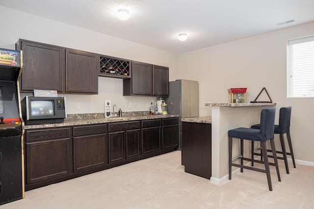 kitchen featuring light colored carpet, a kitchen bar, sink, and dark brown cabinetry