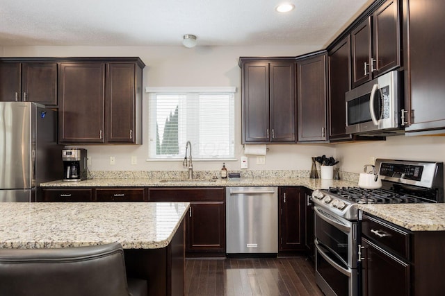 kitchen with stainless steel appliances, sink, light stone counters, and dark brown cabinetry