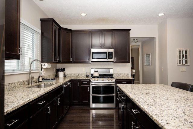 kitchen featuring light stone countertops, appliances with stainless steel finishes, sink, and dark brown cabinetry