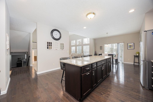 kitchen featuring pendant lighting, stainless steel refrigerator, a kitchen bar, a center island, and dark brown cabinets