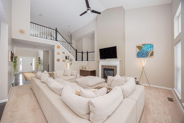 carpeted living room with a tiled fireplace, high vaulted ceiling, and ceiling fan