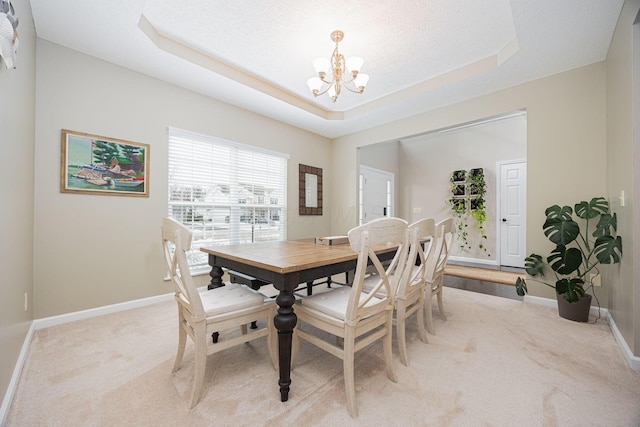 dining space with light carpet, a raised ceiling, and a chandelier