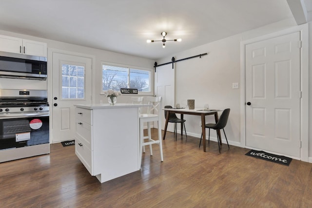 kitchen with dark wood-type flooring, a breakfast bar, a barn door, white cabinets, and appliances with stainless steel finishes