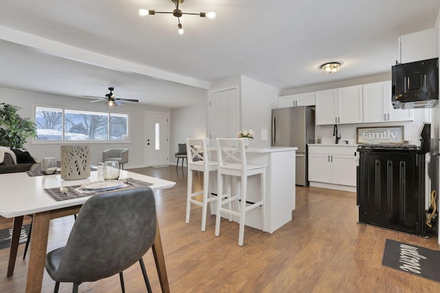 kitchen featuring light hardwood / wood-style flooring, stainless steel fridge, white cabinetry, ceiling fan, and a kitchen breakfast bar