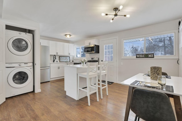 kitchen featuring a kitchen breakfast bar, appliances with stainless steel finishes, a center island, stacked washer and clothes dryer, and white cabinetry