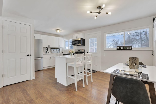 kitchen featuring white cabinets, a center island, a kitchen bar, light wood-type flooring, and appliances with stainless steel finishes