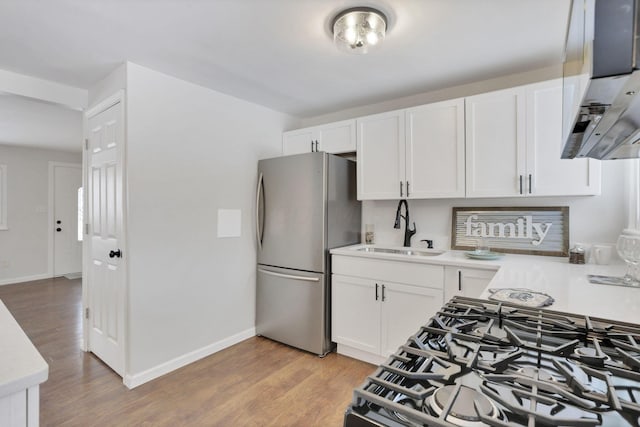 kitchen featuring sink, white cabinetry, gas range oven, light hardwood / wood-style floors, and stainless steel fridge