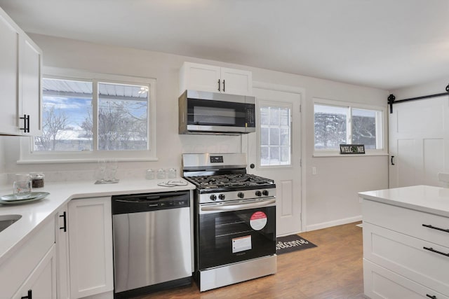 kitchen with appliances with stainless steel finishes, a barn door, light hardwood / wood-style floors, and white cabinetry