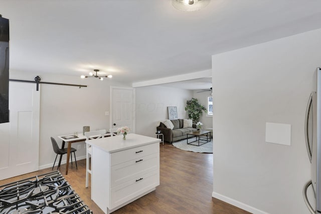 kitchen with a barn door, ceiling fan, stainless steel fridge, dark wood-type flooring, and white cabinets