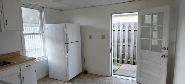 kitchen with white refrigerator, a drop ceiling, and white cabinets