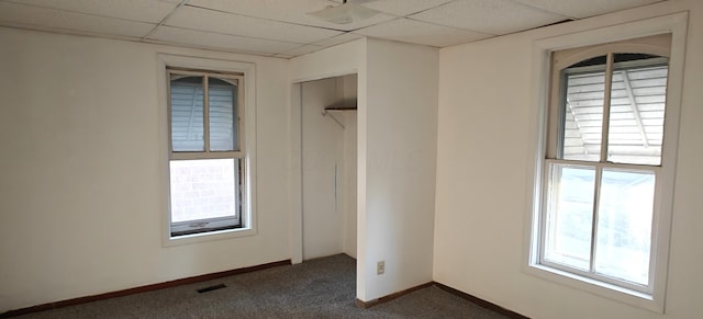 unfurnished bedroom with a paneled ceiling, a closet, and dark colored carpet