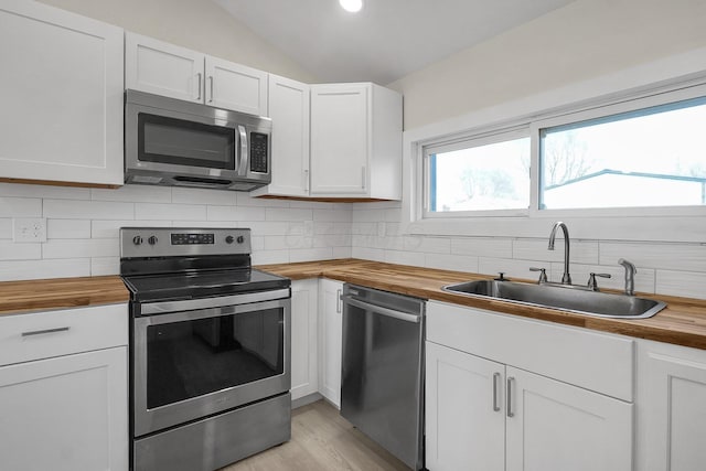 kitchen with vaulted ceiling, stainless steel appliances, wood counters, white cabinets, and sink