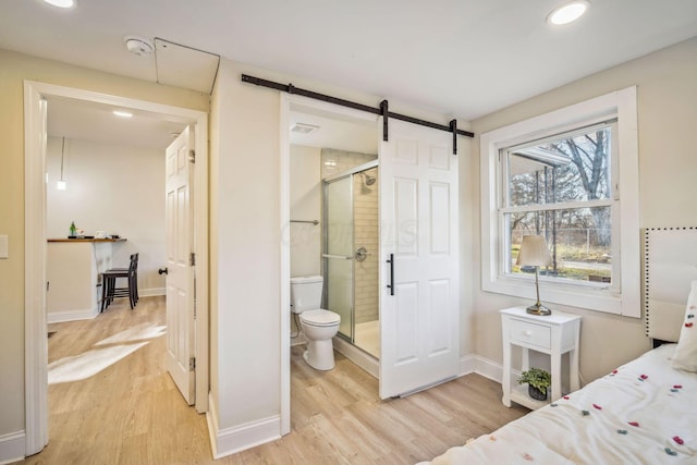 bedroom with ensuite bath, light wood-type flooring, and a barn door