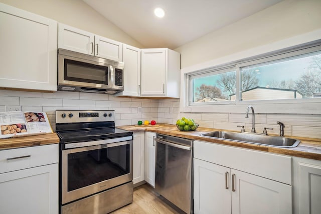 kitchen with stainless steel appliances, sink, white cabinets, lofted ceiling, and wooden counters