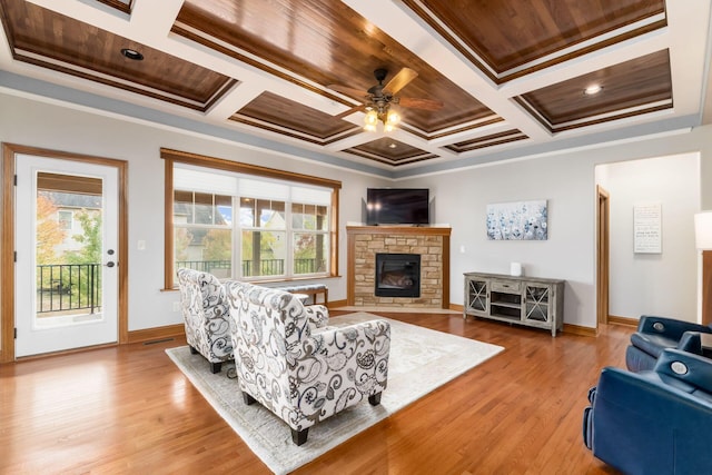 living room with a fireplace, ornamental molding, coffered ceiling, ceiling fan, and light hardwood / wood-style floors