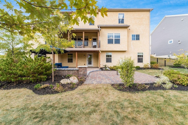 back of house featuring a lawn, a patio, and a balcony