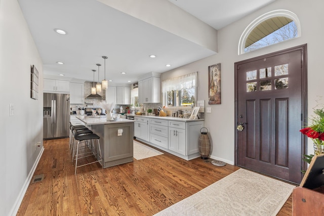 kitchen with decorative backsplash, stainless steel fridge with ice dispenser, a center island, hanging light fixtures, and a breakfast bar area