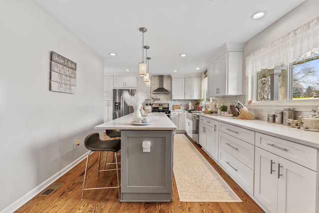 kitchen with a kitchen breakfast bar, stainless steel appliances, wall chimney range hood, white cabinets, and a kitchen island