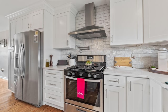 kitchen featuring white cabinetry, wall chimney exhaust hood, stainless steel appliances, tasteful backsplash, and light hardwood / wood-style flooring