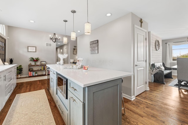 kitchen featuring stainless steel microwave, a kitchen island, dark hardwood / wood-style floors, and decorative light fixtures