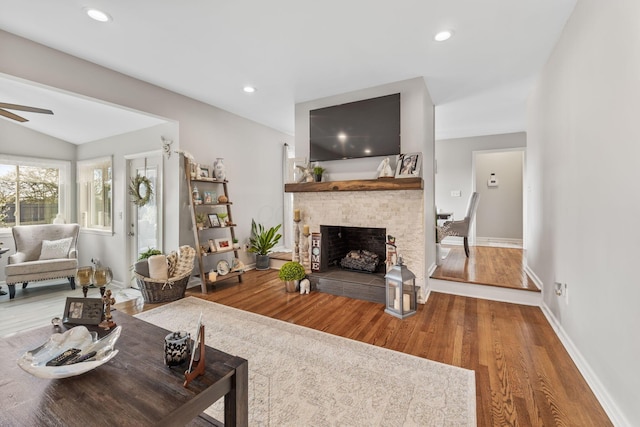 living room with hardwood / wood-style floors, ceiling fan, a stone fireplace, and vaulted ceiling