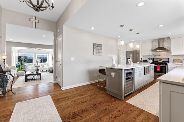 kitchen with pendant lighting, a center island with sink, wall chimney exhaust hood, stainless steel appliances, and beverage cooler