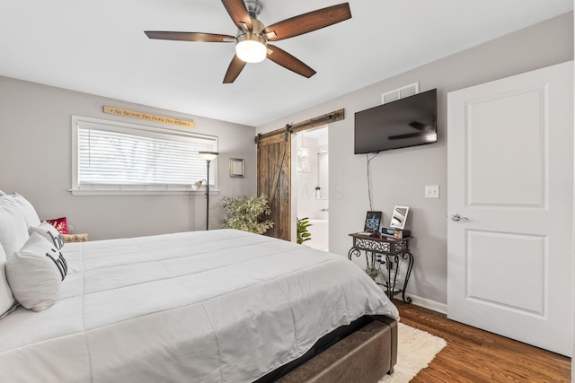 bedroom featuring a barn door, ceiling fan, dark wood-type flooring, and connected bathroom