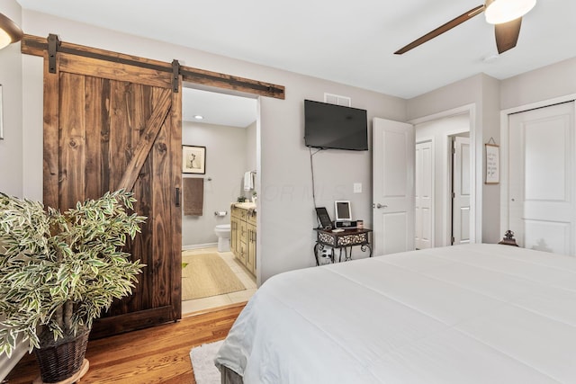 bedroom featuring connected bathroom, a barn door, ceiling fan, and light hardwood / wood-style floors