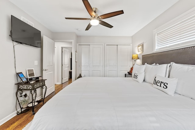 bedroom with hardwood / wood-style flooring, ceiling fan, and multiple closets