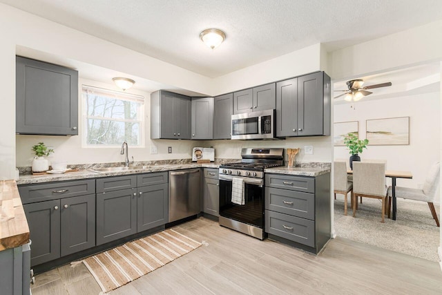 kitchen featuring gray cabinets, light hardwood / wood-style floors, stainless steel appliances, a textured ceiling, and sink