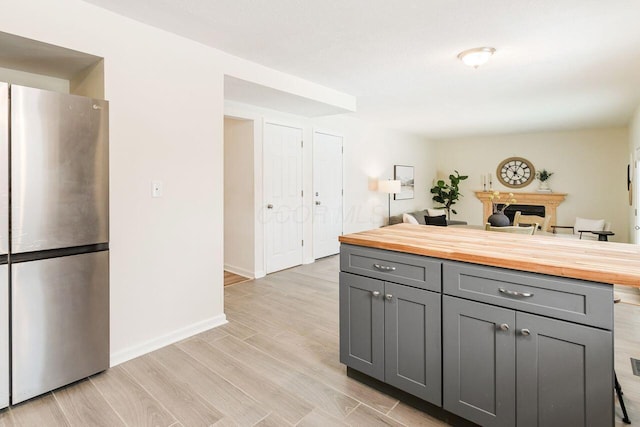 kitchen featuring butcher block countertops, stainless steel refrigerator, gray cabinetry, and light hardwood / wood-style flooring