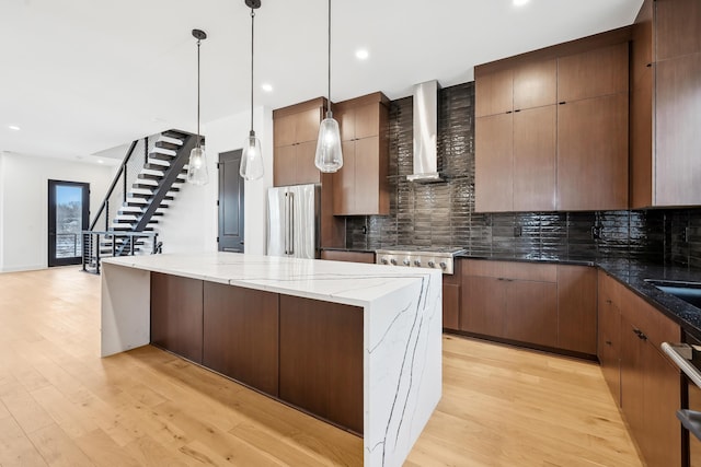 kitchen featuring decorative backsplash, dark stone counters, stainless steel appliances, wall chimney range hood, and light hardwood / wood-style flooring