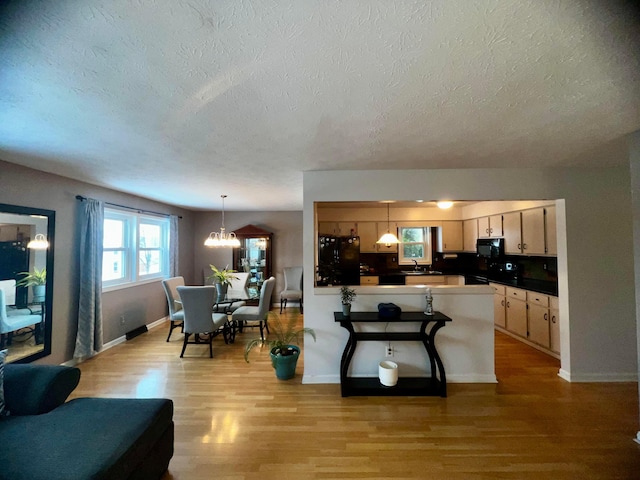 kitchen featuring kitchen peninsula, a chandelier, pendant lighting, light hardwood / wood-style floors, and black appliances