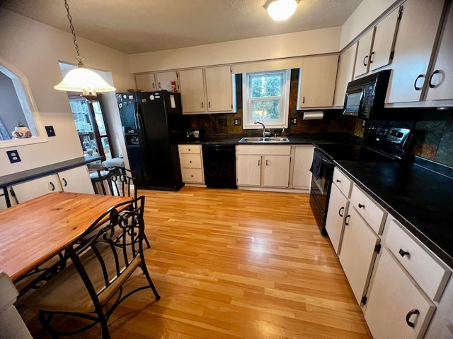 kitchen featuring hanging light fixtures, black appliances, decorative backsplash, light wood-type flooring, and sink