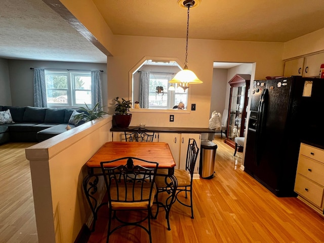 kitchen with kitchen peninsula, light hardwood / wood-style flooring, decorative light fixtures, black refrigerator with ice dispenser, and light brown cabinets