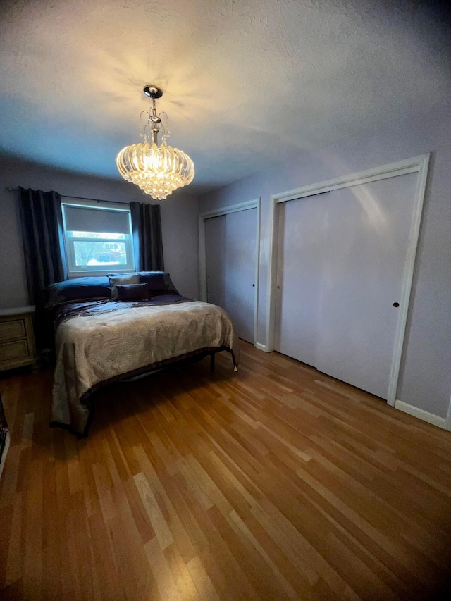 bedroom with two closets, wood-type flooring, and a chandelier