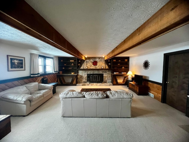 carpeted living room featuring built in shelves, a textured ceiling, wooden walls, and a stone fireplace