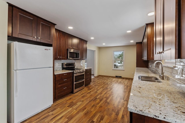 kitchen featuring appliances with stainless steel finishes, light stone counters, sink, and wood-type flooring