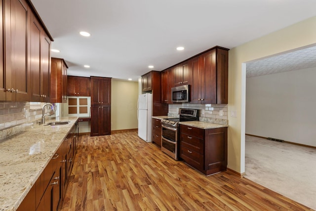 kitchen featuring stainless steel appliances, light stone counters, decorative backsplash, sink, and light hardwood / wood-style flooring