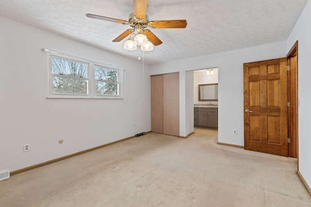 unfurnished bedroom with ceiling fan, light colored carpet, connected bathroom, and a textured ceiling